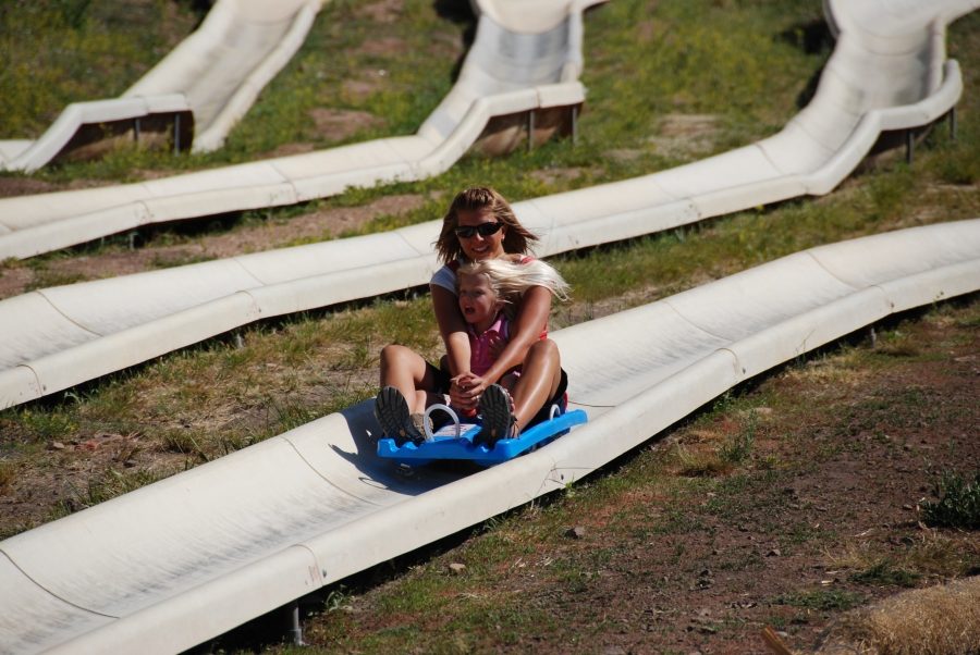 A rider in sunglasses steering a blue sled through a banked curve on a concrete alpine slide