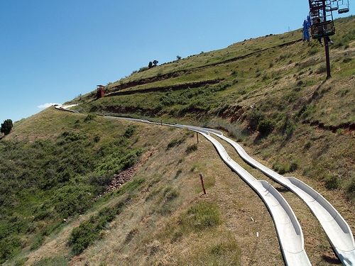 Twin concrete alpine slide tracks curving down a grassy hillside below a chairlift
